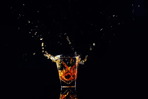 黒の背景にスプラッシュとウイスキーの分離ショット グラスにブランデーします — ストック写真