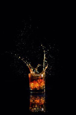 Siyah arka planda su sıçramış viski, bardakta brendi.