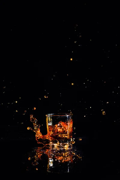 Whiskey con salpicadura sobre fondo negro, brandy en un vaso — Foto de Stock