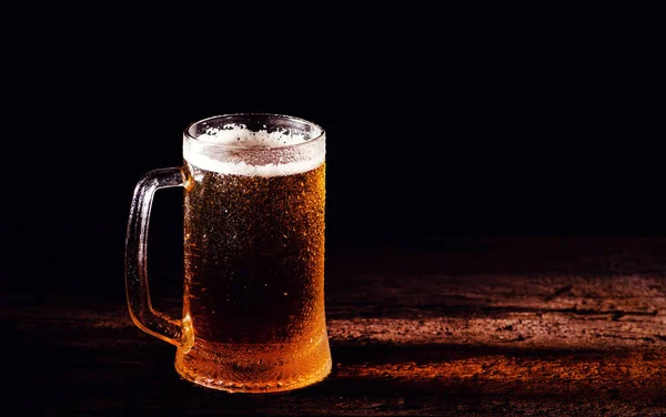 ビールだ 黒い背景の上に木製のテーブルの上に水滴のあるガラスの中の冷たいクラフトライトビール — ストック写真