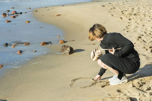 Schöne Mädchen zeichnet auf dem Sand Herz — Stockfoto