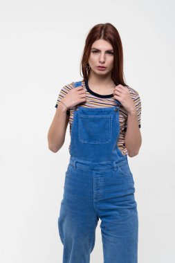 Stüdyoda poz veren genç ve güzel bir kız, mavi tulumlar içinde duruyor.