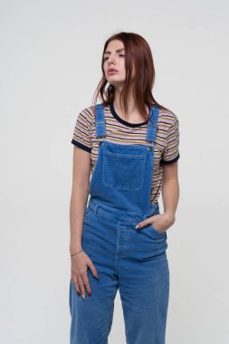 Genç ve güzel bir kız mavi tulumlar içinde duruyor.