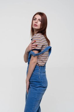 Stüdyoda poz veren genç, güzel bir kadın, mavi tulumlar içinde duruyor.