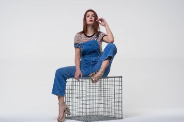 Mavi tulumlu, metal bir Gabion 'un üzerinde oturan genç ve güzel bir kız.