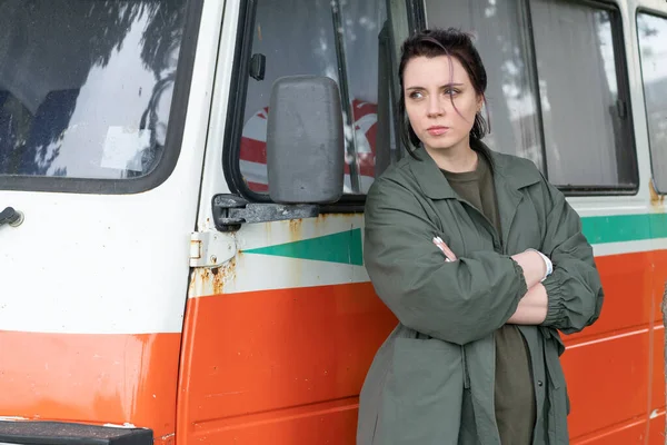 young beautiful girl posing near an old orange car in a green cloak outside