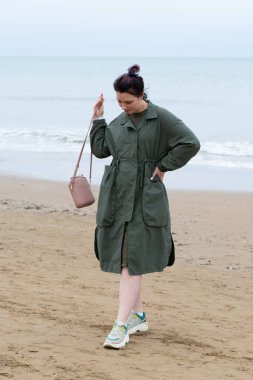 Deniz kenarında yeşil ceketli bir kız var.