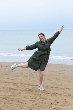 Genç ve güzel bir kız denizin kenarında yağmurlukla duruyor.