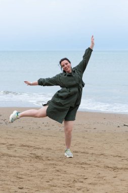 Genç ve güzel bir kız denizin kenarında yağmurlukla duruyor.