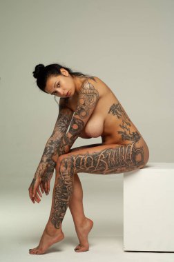 Dövmeli genç kız stüdyoda çıplak poz veriyor.