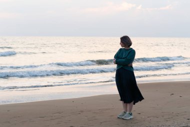 Kız deniz kıyısında kazakla duruyor.