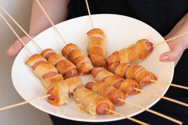 Hamurdaki sosisler beyaz tabakta yatıyor.