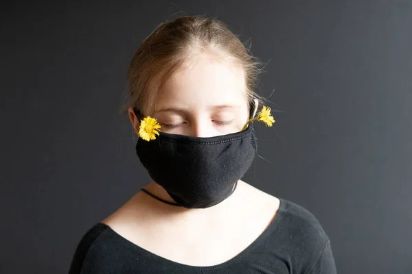 little girl stands in a black medical mask in the studio, stands near a black wall