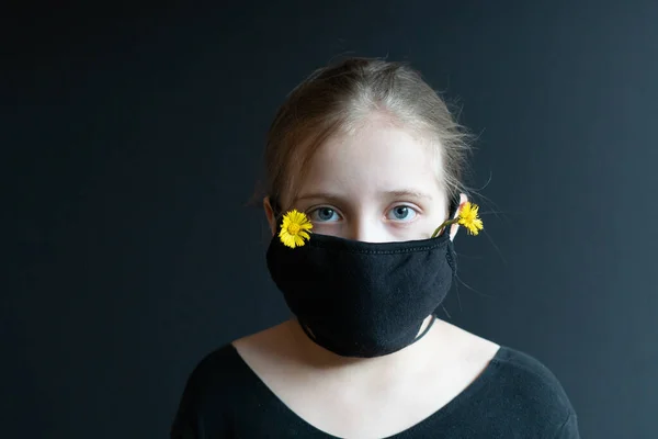 little girl stands in a black medical mask in the studio, stands near a black wall