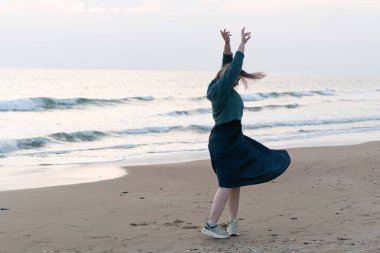Kız deniz kıyısında kazakla dans ediyor.