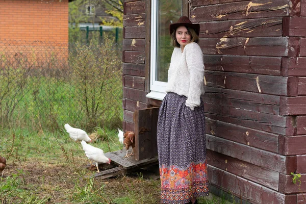 a village girl stands in a village near chickens
