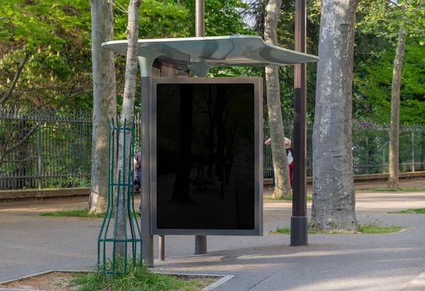 Bus stop billboard Mockup in empty street in Paris. Parisian style hoarding advertisement close to a park in beautiful city