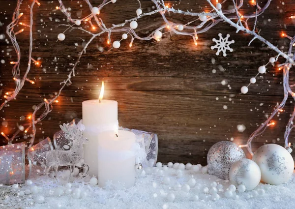 雪とクリスマス ライト クリスマス装飾的なボールと鹿と 2 つのろうそく。木製の背景のクリスマスの装飾。お祝いクリスマス背景 — ストック写真