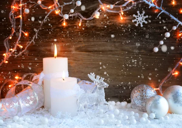 Dos velas encendidas con un ciervo con bolas decorativas de Navidad en la nieve y las luces de Navidad. Decoraciones navideñas sobre fondo de madera. Fondo navideño festivo — Foto de Stock