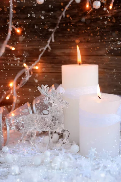 Dvě hořící svíčky s jelenem na sněhu a vánoční osvětlení. Vánoční ozdoby na dřevěné pozadí. Slavnostní vánoční pozadí — Stock fotografie
