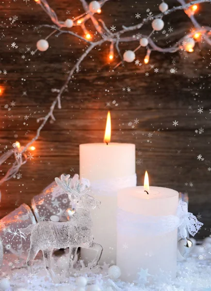 Zwei brennende Kerzen mit einem Hirsch auf Schnee und Weihnachtsbeleuchtung. Weihnachtsdekoration auf Holzgrund. festlicher weihnachtlicher Hintergrund — Stockfoto