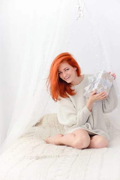 Lachende gelukkige vrouw met geschenkdoos zittend op het bed en camera te kijken — Stockfoto