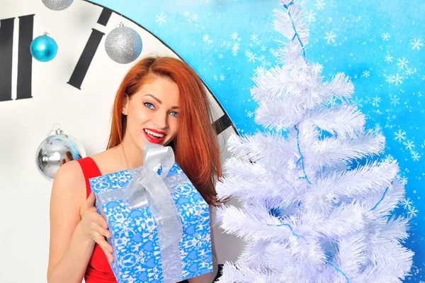 크리스마스 선물 상자를 크리스마스 트리 옆에 두고 있는 젊은 여성의 웃는 모습 — 스톡 사진