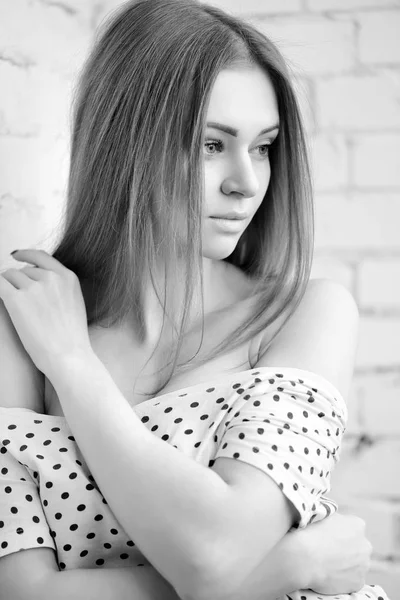 Retrato preto e branco de uma bela fêmea. Jovem mulher atraente de pé perto de uma parede de tijolo branco . — Fotografia de Stock
