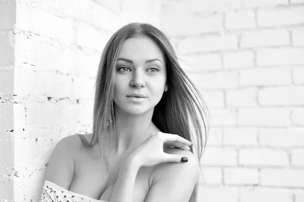 Black and white portrait of a beautiful female. Attractive young woman standing near a white brick wall.