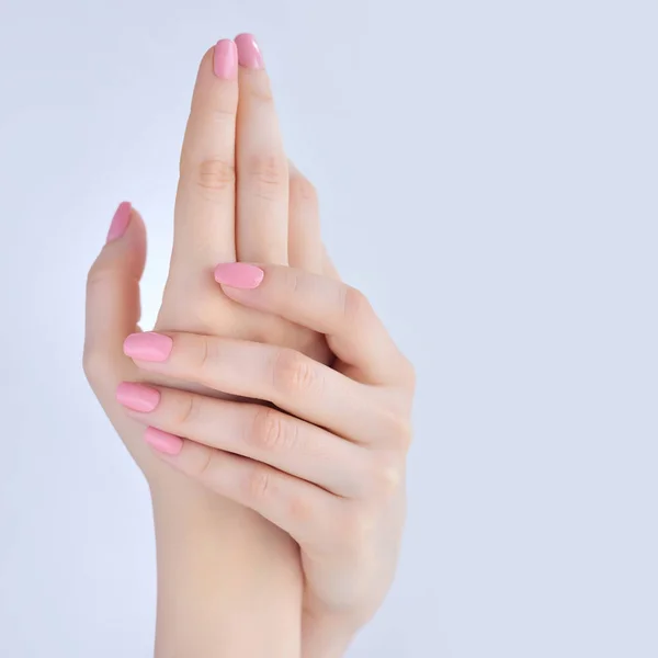 Close-up van handen van een jonge vrouw met roze manicure op nagels tegen witte achtergrond — Stockfoto