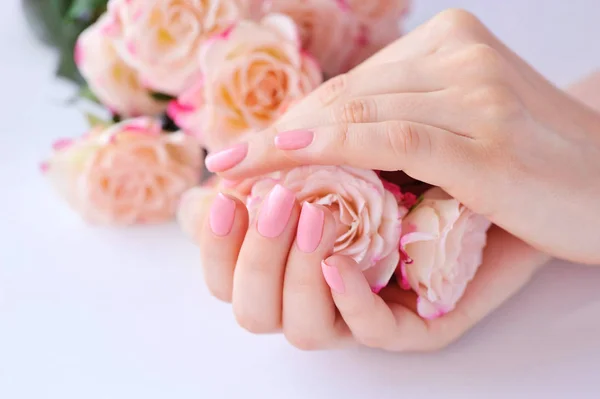 Handen van een vrouw met roze manicure nagels en rozen — Stockfoto