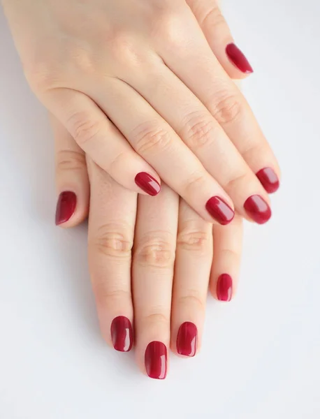 Nahaufnahme der Hände einer jungen Frau mit roter Maniküre auf Nägeln vor weißem Hintergrund — Stockfoto