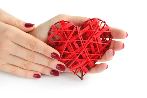Rieten rood hart in handen van de vrouw op witte achtergrond. Closeup hart in hand van meisje met rode manicure. Happy Valentines day, liefde concept. — Stockfoto