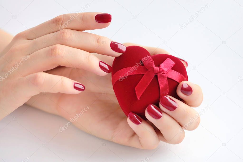 Beautiful female hands with red manicure holding a box of heart-shaped. Happy Valentines day, love concept.
