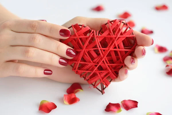 Coração vermelho de vime nas mãos da mulher sobre fundo branco. Coração fechado na mão de menina com manicura vermelha. Feliz Dia dos Namorados, conceito de amor . — Fotografia de Stock