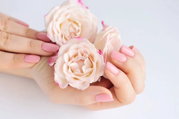 Handen van een vrouw met roze manicure nagels en rozen — Stockfoto