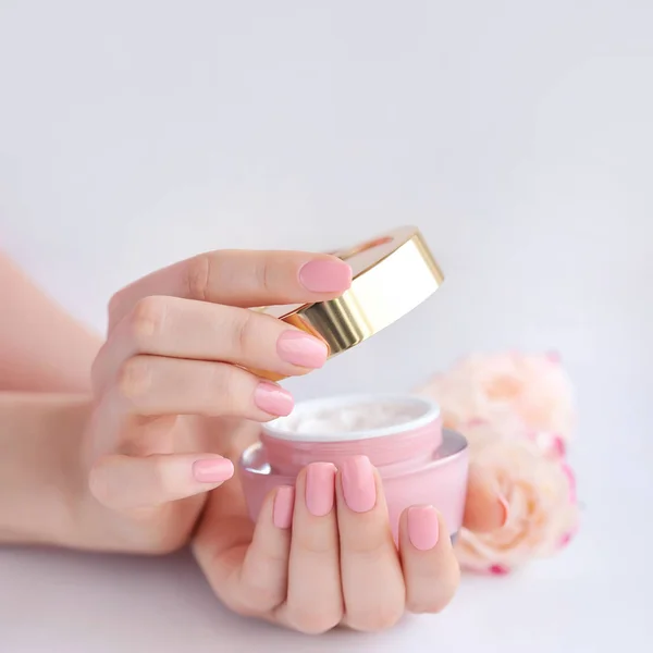 Mãos de uma mulher com manicure rosa com creme — Fotografia de Stock