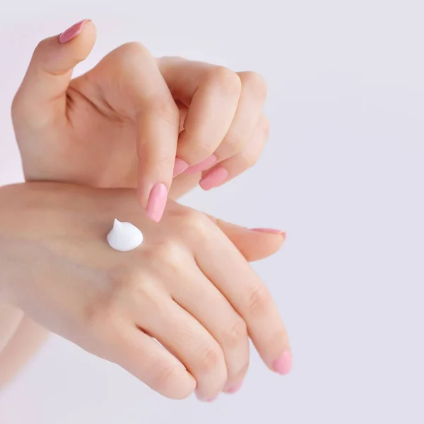 Mujer joven con manicura rosa aplica crema en sus manos — Foto de Stock