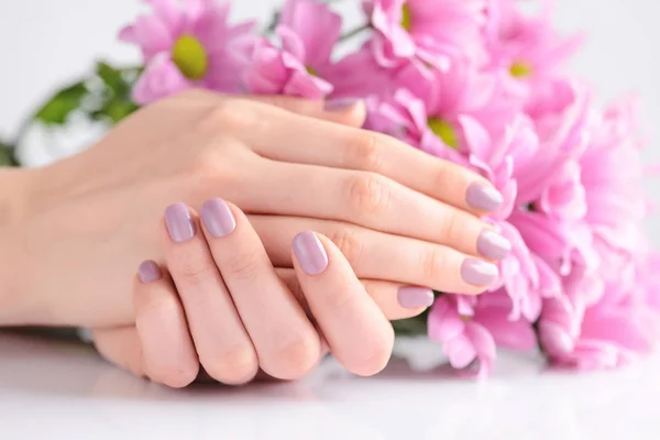 Τα χέρια της μια γυναίκα με ροζ μανικιούρ για τα νύχια και τα ροζ λουλούδια — Φωτογραφία Αρχείου