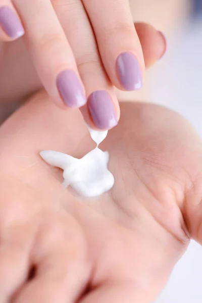 Jonge vrouw met roze manicure geldt crème op haar handen. Close-up — Stockfoto