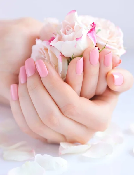 Mani di una donna con manicure rosa su unghie e rose — Foto Stock