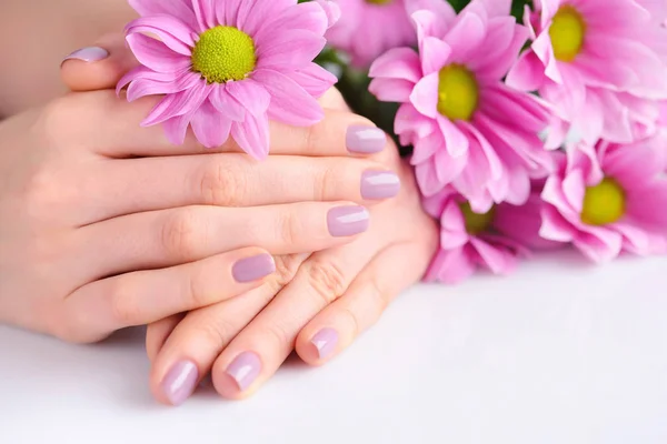 Händerna på en kvinna med rosa manikyr på naglarna och rosa blommor — Stockfoto