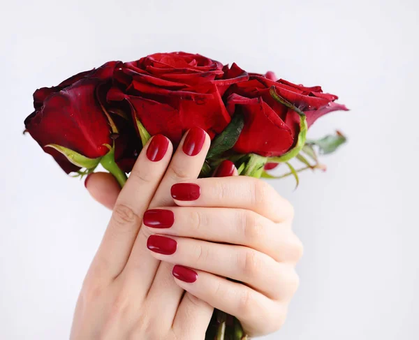 Mãos de uma mulher com manicure vermelho escuro com um buquê de rosas vermelhas — Fotografia de Stock