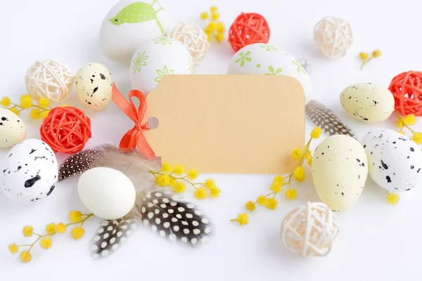 Easter eggs and mimosa flowers on white background with blank card to greet — Stock Photo, Image