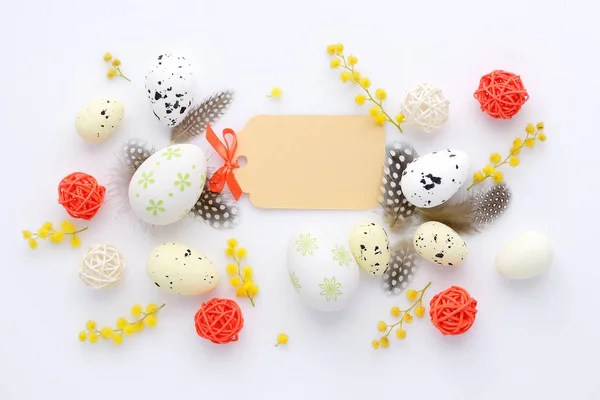 Ovos de Páscoa e flores mimosa no fundo branco com cartão em branco para cumprimentar. Vista superior . — Fotografia de Stock