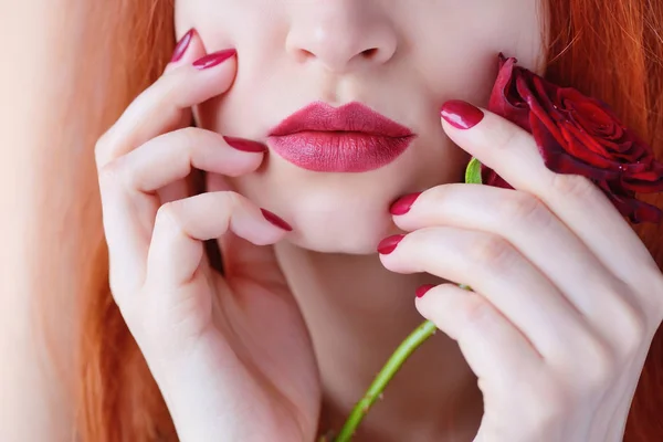 Portrait avec fleur de rose rouge. Des lèvres et des ongles rouges. Belle jeune femme rousse . — Photo