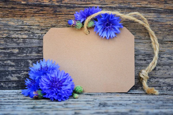 Etiqueta de papel con acianos frescos (Centaurea cyanus) sobre mesa de madera —  Fotos de Stock