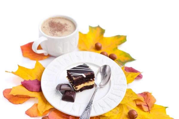 Piece of cake on a plate, chocolate, autumn leaves, nuts and a cup of coffee — Stock Photo, Image