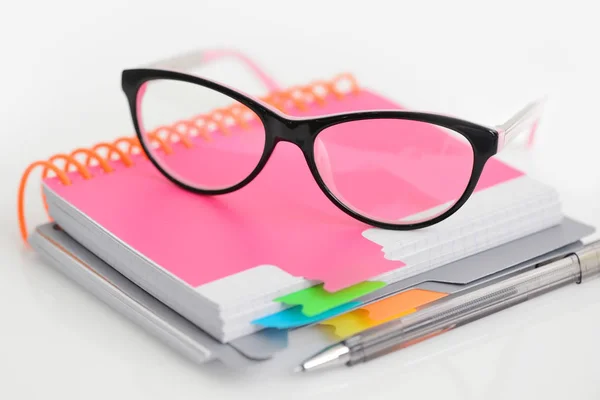 Óculos de olho com caneta e caderno espiral em branco sobre fundo branco — Fotografia de Stock