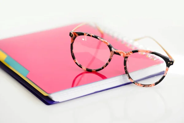 Eye glasses with pink spiral notebook on white background Royalty Free Stock Images